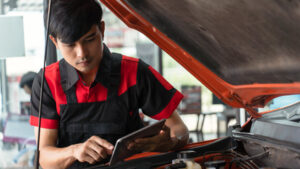 young asian male employee using computer to check engine operation employee repairing engine auto repair using diagnostic technology